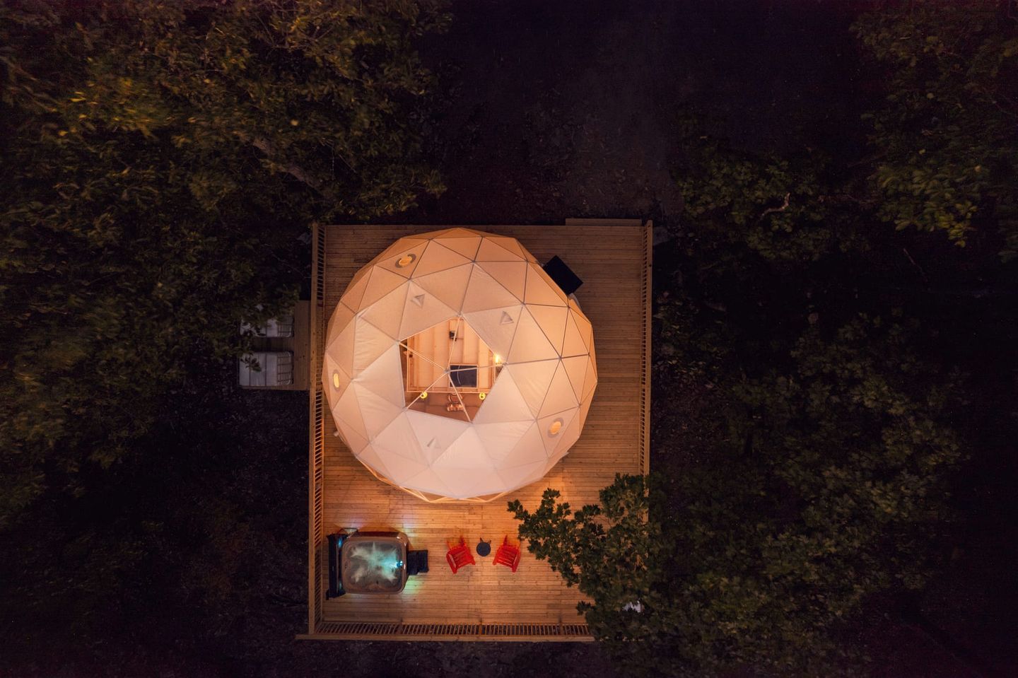 A dome-shaped structure with a central seating area, surrounded by a wooden deck, and a pool with a hot tub.