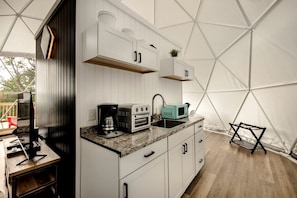 A compact kitchen with white cabinets, a countertop, a sink, a coffee maker, a toaster, and a microwave.