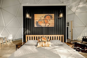 A bedroom with a wooden bed, two wall-mounted lanterns, a wooden horse painting, and a cowhide rug. - Stunning Dome with Barbecue and Hot-tub in Capon Bridge, West Virginia (Capon Bridge)