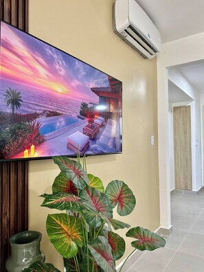 A television mounted on a wall displaying a sunset scene with a pool and lounge area. - Modern Stay / FREE Airport Pickup & Beach Shuttle (Punta Cana)