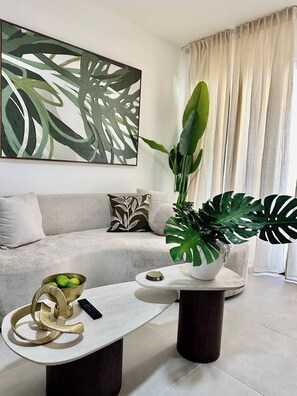 A modern living room with a sofa, a coffee table, a plant, and a painting. - Modern Stay / FREE Airport Pickup & Beach Shuttle (Punta Cana)