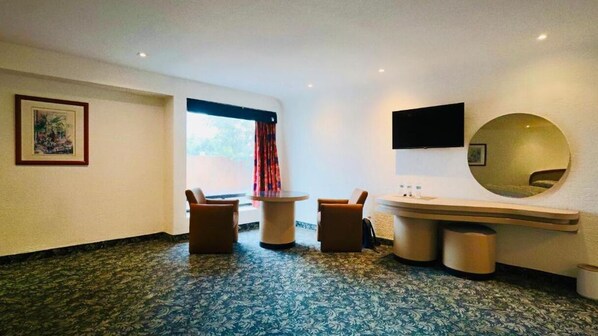 Una habitación de hotel con una cama, un espejo redondo, un televisor y una pequeña mesa con sillas.