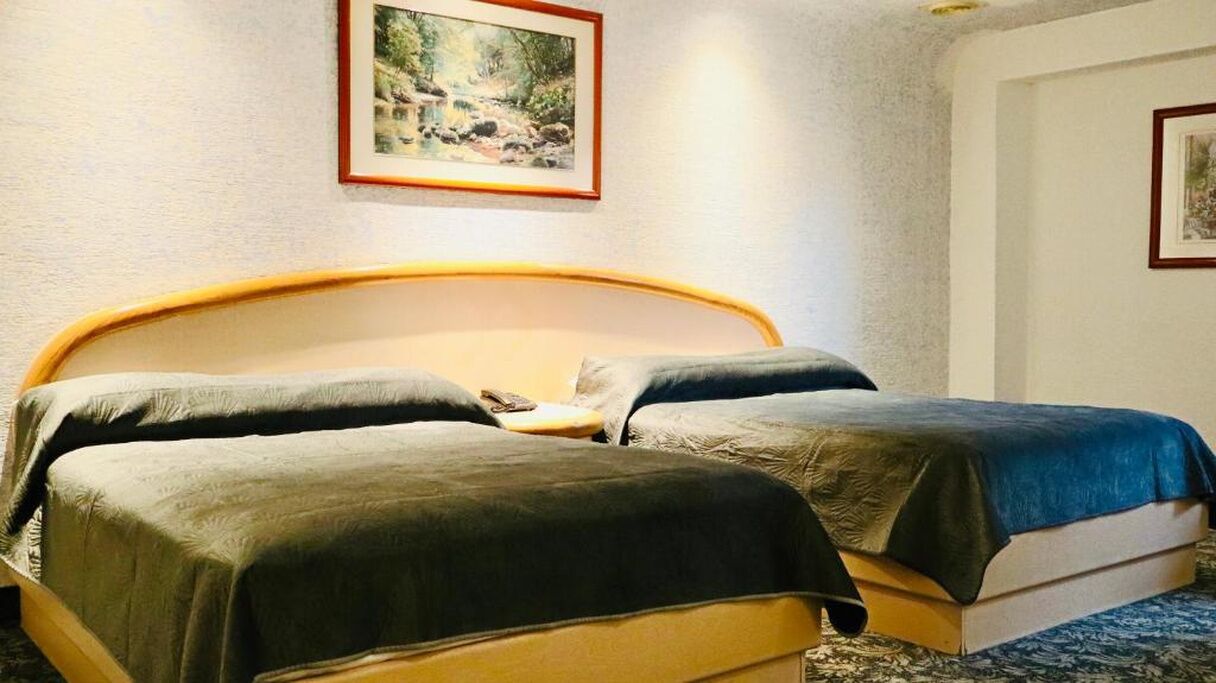 Una cama doble con cabecera de madera, dos almohadas y una manta azul.
