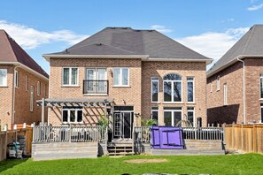 Ein zweigeschossiges Backsteinhhaus mit überdachter Terrasse, einem eingezäunten Garten und einem violetten Lagercontainer.