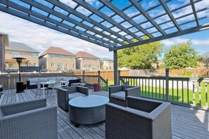 Katettu ulkoterassi, jossa on rottinkihuonekaluja, pyöreä pöytä ja pergola.