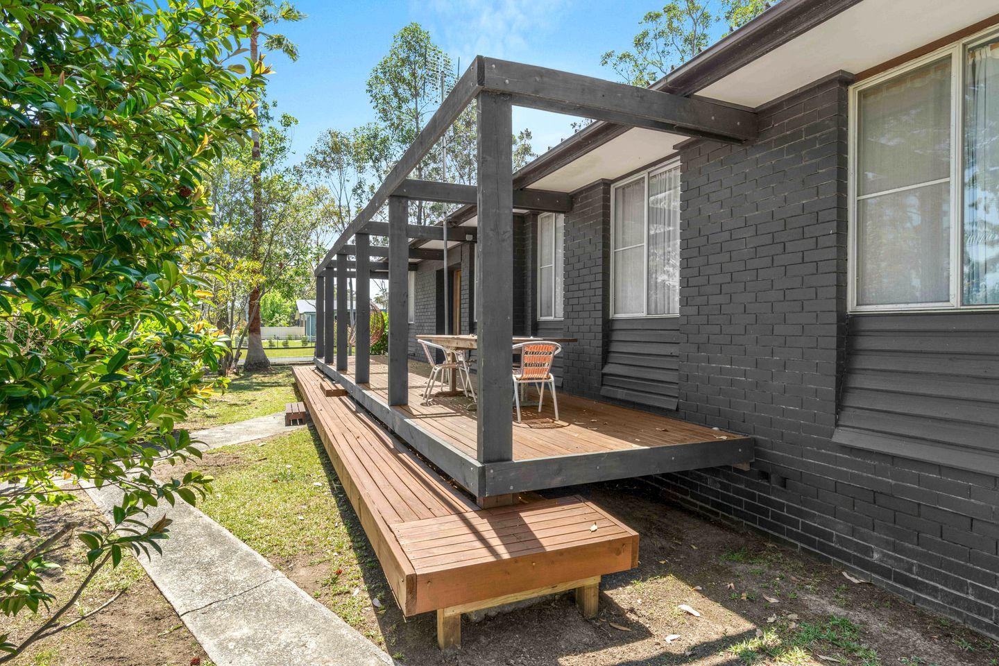 A house with a wooden deck, a bench, and a table with chairs.