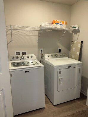 A laundry area with two white Maytag washers and dryers, a metal shelf with laundry supplies, and a hanging iron. - 3-bedroom townhome in delightful Falling Waters with AC (Falling Waters)