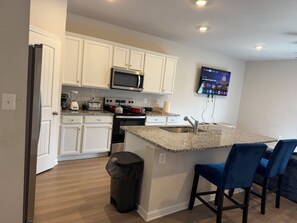 A modern kitchen with white cabinetry, a granite countertop, a stainless steel sink, a microwave, a stove, and a trash can. - 3-bedroom townhome in delightful Falling Waters with AC (Falling Waters)