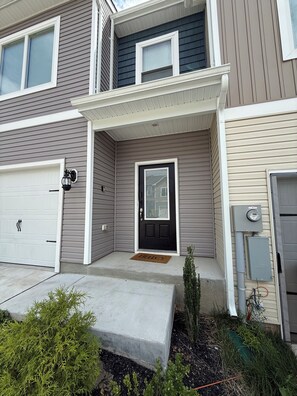 A two-story residential building with a front door, garage, and a small front yard with a welcome mat. - 3-bedroom townhome in delightful Falling Waters with AC (Falling Waters)