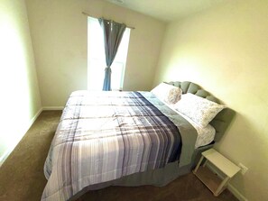 A bedroom with a bed, a nightstand, a window with curtains, and a carpeted floor. - 3-bedroom townhome in delightful Falling Waters with AC (Falling Waters)