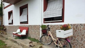 Ein Gebäude mit steinverkleideter Fassade, eine Bank, ein Fahrrad mit Korb und eine kleine Gartenanlage.
