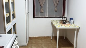 Eine Küche mit Kühlschrank, einem Tisch mit gemustertem Tischläufer und einem Fenster mit Vorhängen.