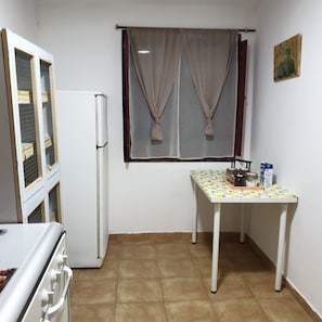 Ett kök med ett kylskåp, ett bord med ett mönstrat bordsduks och ett fönster med gardiner.
