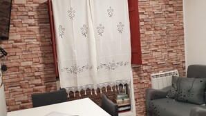 Ein Wohnzimmer mit Backsteinwand, einem weißen Tisch mit Fernbedienung, einem grauen Sofa und einem roten Vorhang.