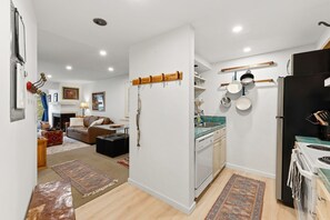 A modern kitchen with white cabinets, a black refrigerator, and a stove. There is a dining area with a brown leather sofa and a coffee table. - Vail Couple's Retreat:  Ski & Golf, Near Village (Vail)