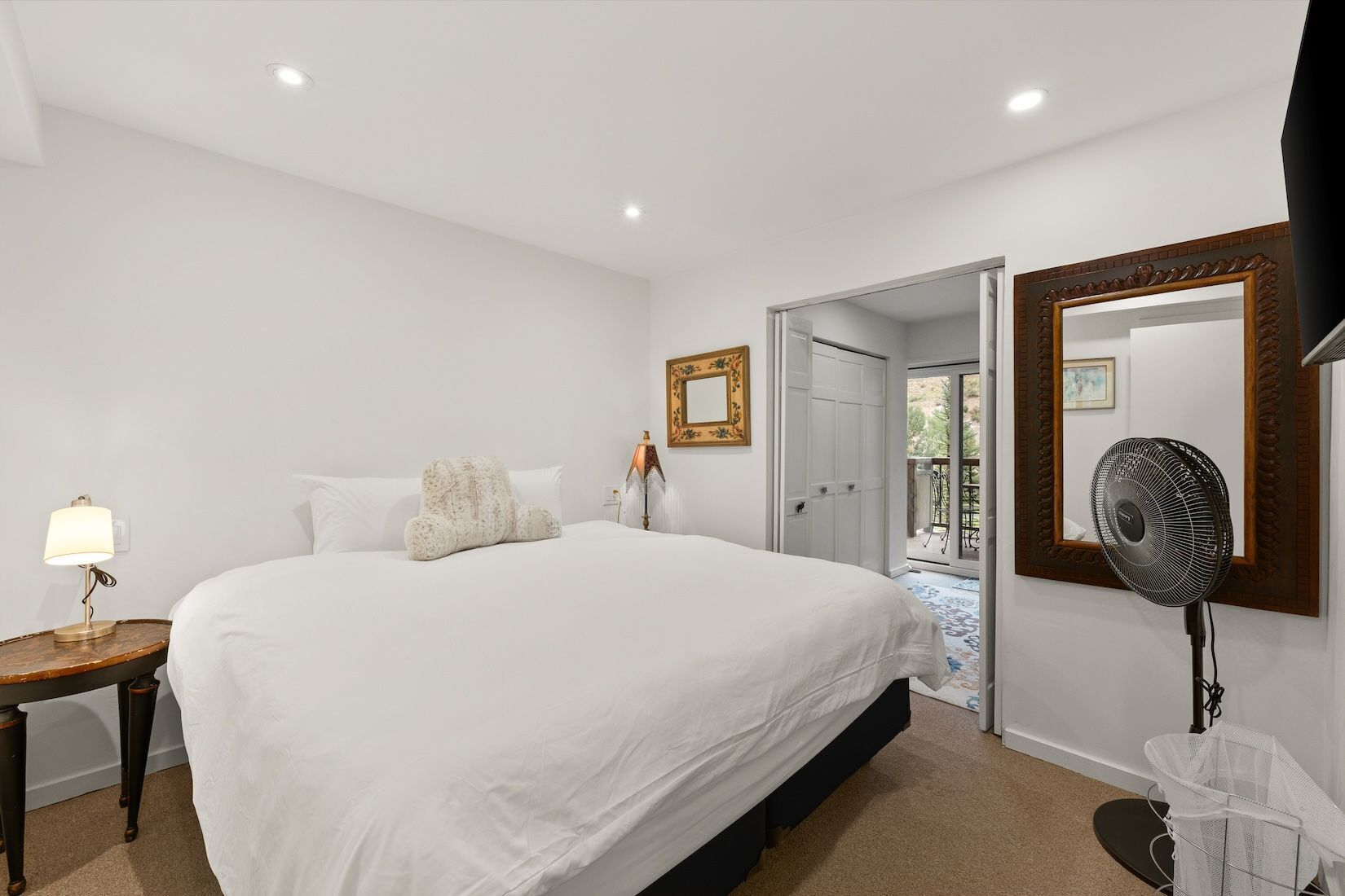 Une chambre à coucher avec un grand lit, une table de chevet avec une lampe, un miroir et un ventilateur.