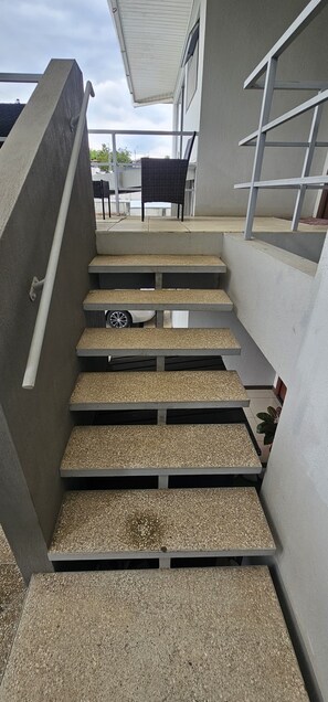 Unos escalones de concreto conducen a un espacio al aire libre cubierto, con una silla y una mesa.