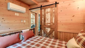 A wooden interior with a bed, pillows, a sliding barn door, and an air conditioning unit.