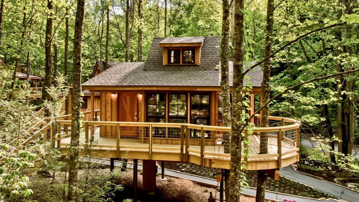A wooden cabin with a circular deck, surrounded by a forest.