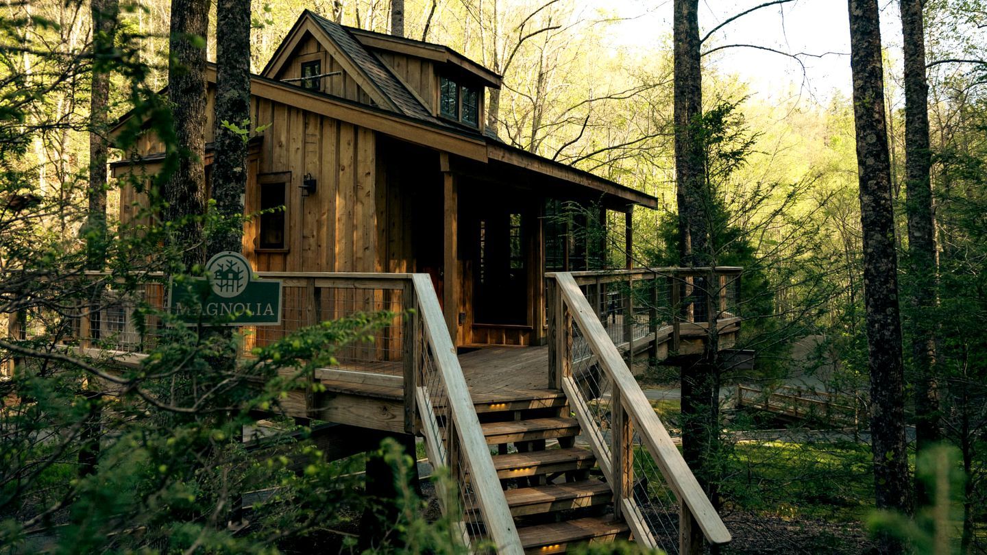 A wooden cabin with a staircase leading to a porch, surrounded by trees.
