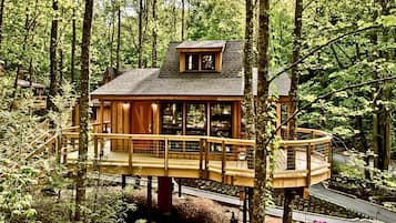 A wooden treehouse with a balcony, surrounded by a forest.