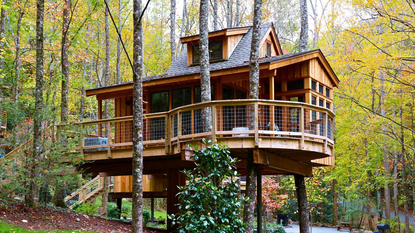 A wooden treehouse with multiple levels, built on stilts, surrounded by a forest.
