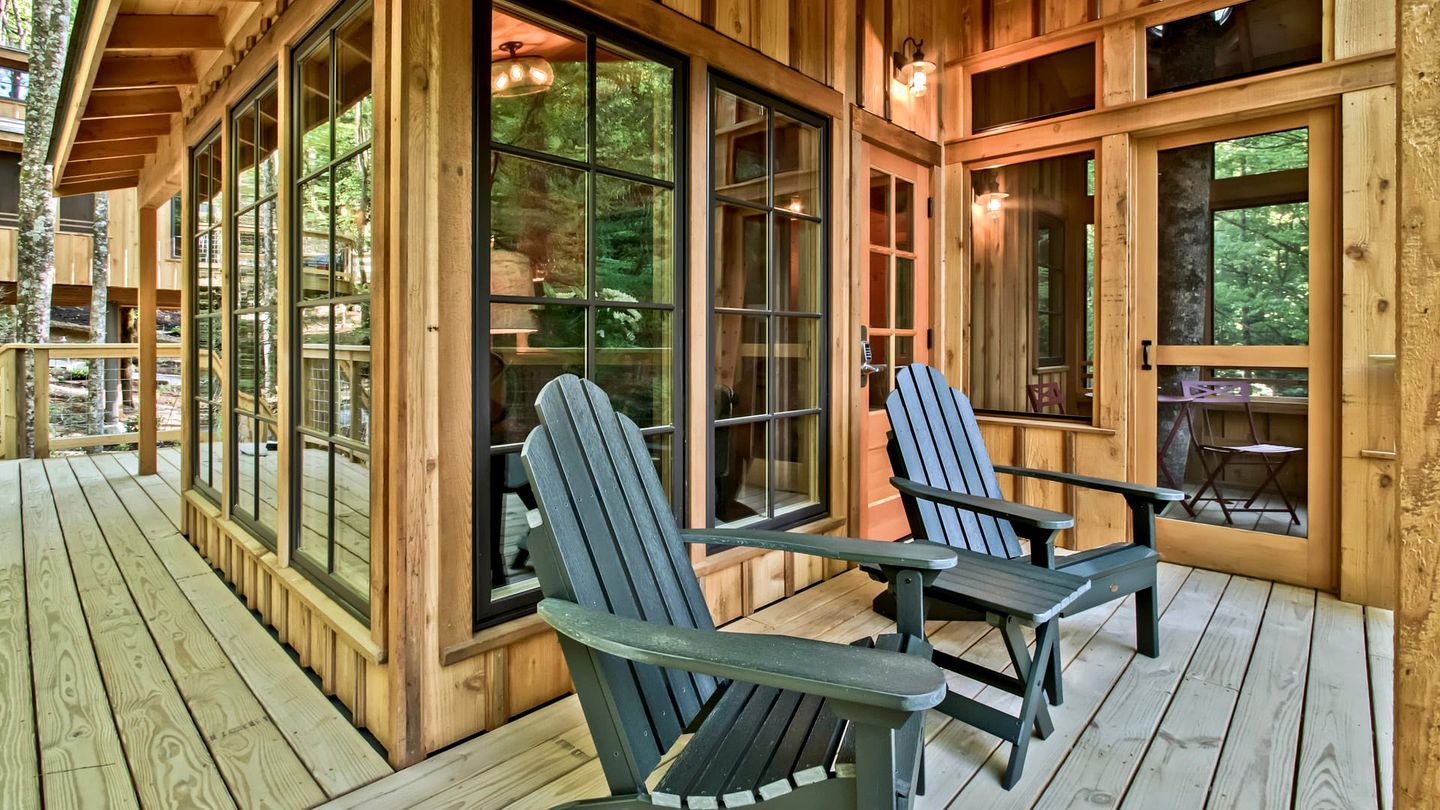 A wooden deck with two Adirondack chairs and large windows.