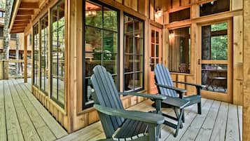 A wooden deck with two Adirondack chairs and large windows.