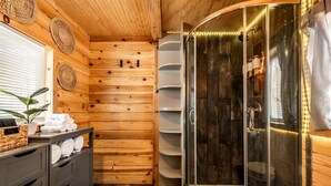 A wooden interior with a glass-enclosed shower, a vanity with towels, and a plant. - Rustic Tiny Home near Garden of the Gods, Perfect for a Weekend Getaway from Colorado Springs (Woodland Park)