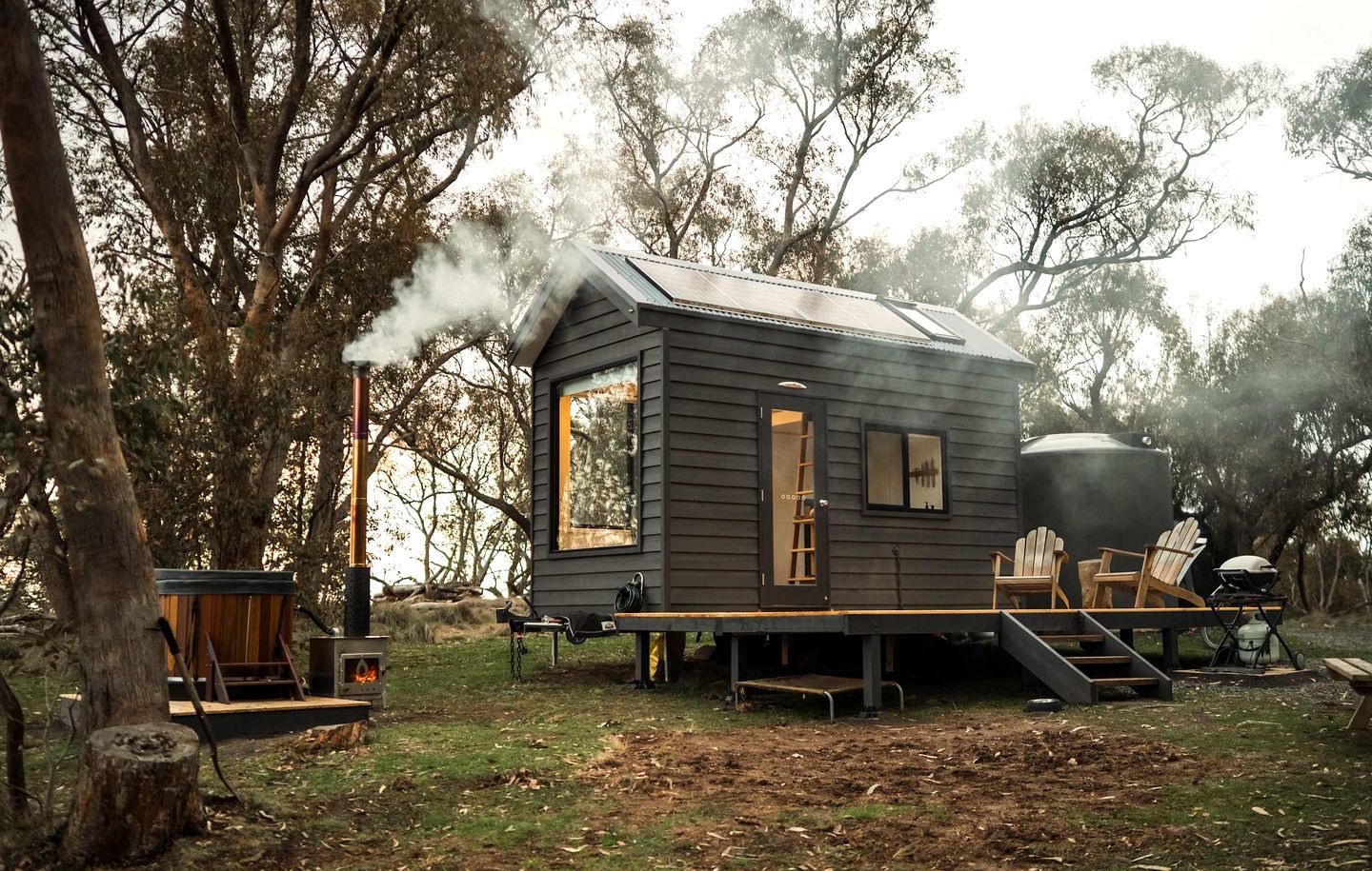 Une cabane avec une cheminée, une terrasse et des sièges d’extérieur.