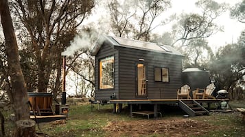 Une cabane avec une cheminée, une terrasse et des sièges d’extérieur.