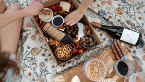 Una caja de diversos bocadillos y una botella de vino sobre un mantel con estampado floral.