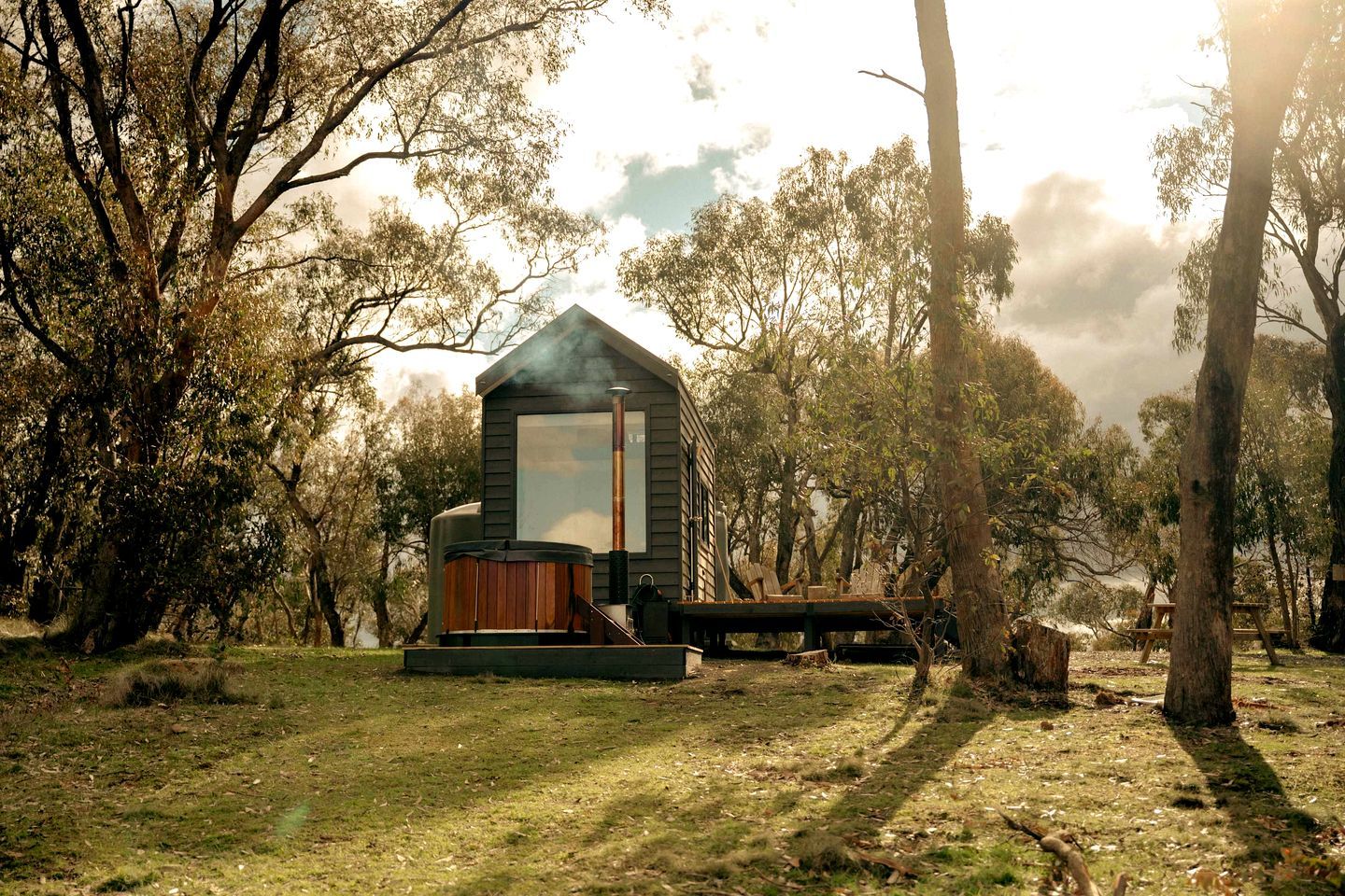 Un chalet rustique doté d’un bain à remous et d’une cheminée, entouré d’arbres.