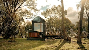 Un chalet rustique doté d’un bain à remous et d’une cheminée, entouré d’arbres.