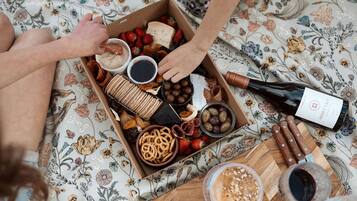 A box of assorted snacks and a bottle of wine on a floral tablecloth.