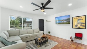 A modern living room with a sofa, a ceiling fan, a red suitcase, and a framed picture on the wall. - Ocean Breeze Cottage: Private Oasis Near Boynton Beach & Delray Beach. (Boynton Beach)