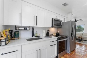 A modern kitchen with white cabinets, a stainless steel refrigerator, a microwave, and a gas stove. - Ocean Breeze Cottage: Private Oasis Near Boynton Beach & Delray Beach. (Boynton Beach)
