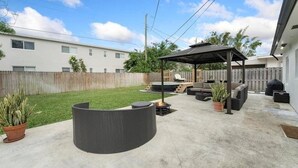 A backyard with a covered patio, outdoor furniture, and a fire pit. - Ocean Breeze Cottage: Private Oasis Near Boynton Beach & Delray Beach. (Boynton Beach)
