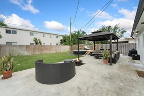 A backyard with a covered patio, outdoor furniture, and a fire pit. - Ocean Breeze Cottage: Private Oasis Near Boynton Beach & Delray Beach. (Boynton Beach)