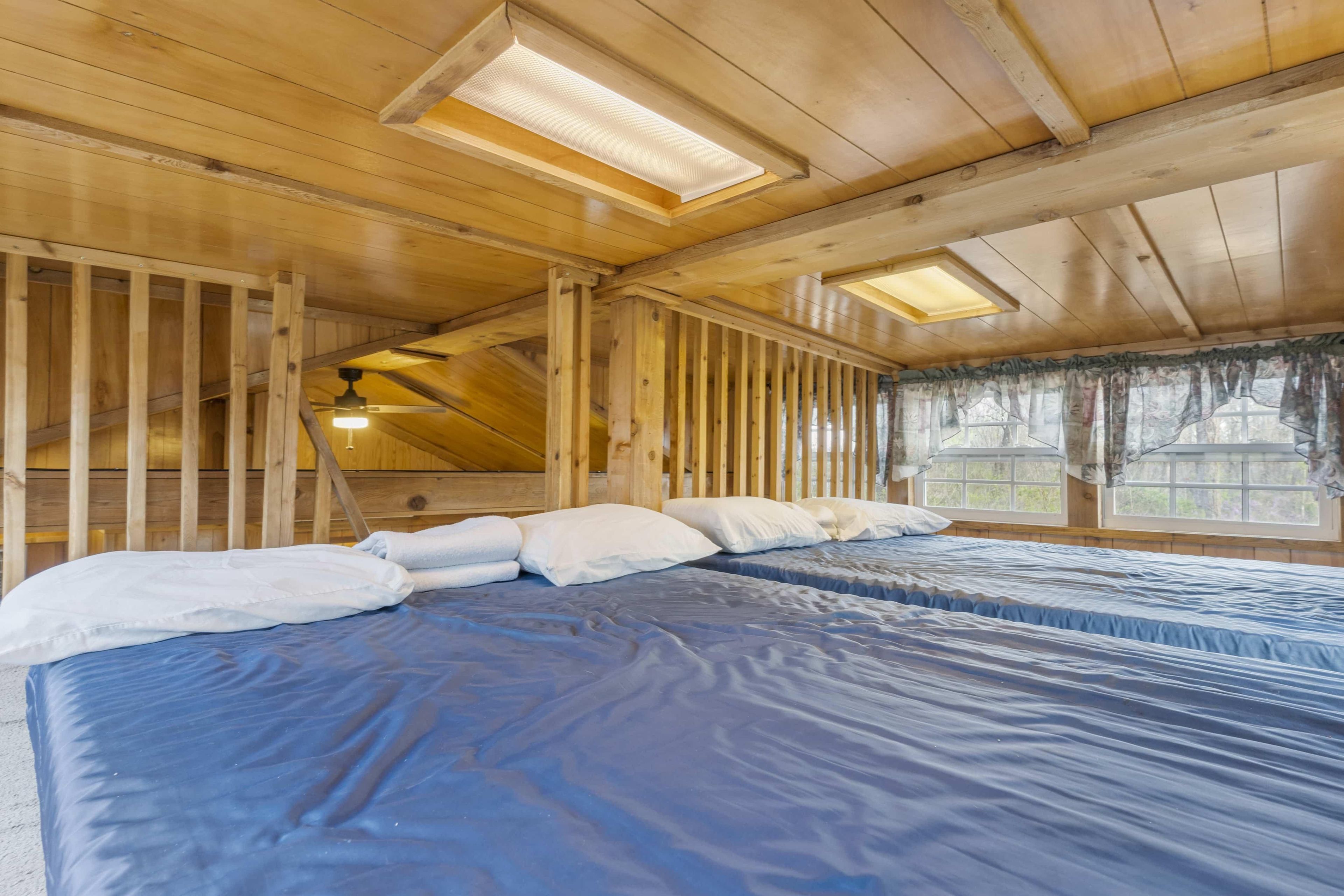 Une chambre avec un grand lit, des poutres apparentes en bois au plafond, des fenêtres de toit et une fenêtre avec des rideaux.