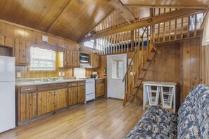 A wooden cabin interior with a kitchen, a dining area, and a staircase. - Deluxe Cabin - Our Deluxe Cabin has two rooms (1 bedroom) with a Queen bed, futon or queen sofa, and 4 twin beds in a loft. Complete with a bathroom, kitchen stocked with dishes, toaster, and coffee pot, fireplace, and screened  porch. Non-smoking. M (Gore)