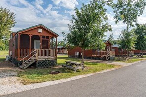 A cabin-style lodging with a porch, a picnic table, and a grill area. - Deluxe Cabin - Our Deluxe Cabin has two rooms (1 bedroom) with a Queen bed, futon or queen sofa, and 4 twin beds in a loft. Complete with a bathroom, kitchen stocked with dishes, toaster, and coffee pot, fireplace, and screened  porch. Non-smoking. M (Gore)