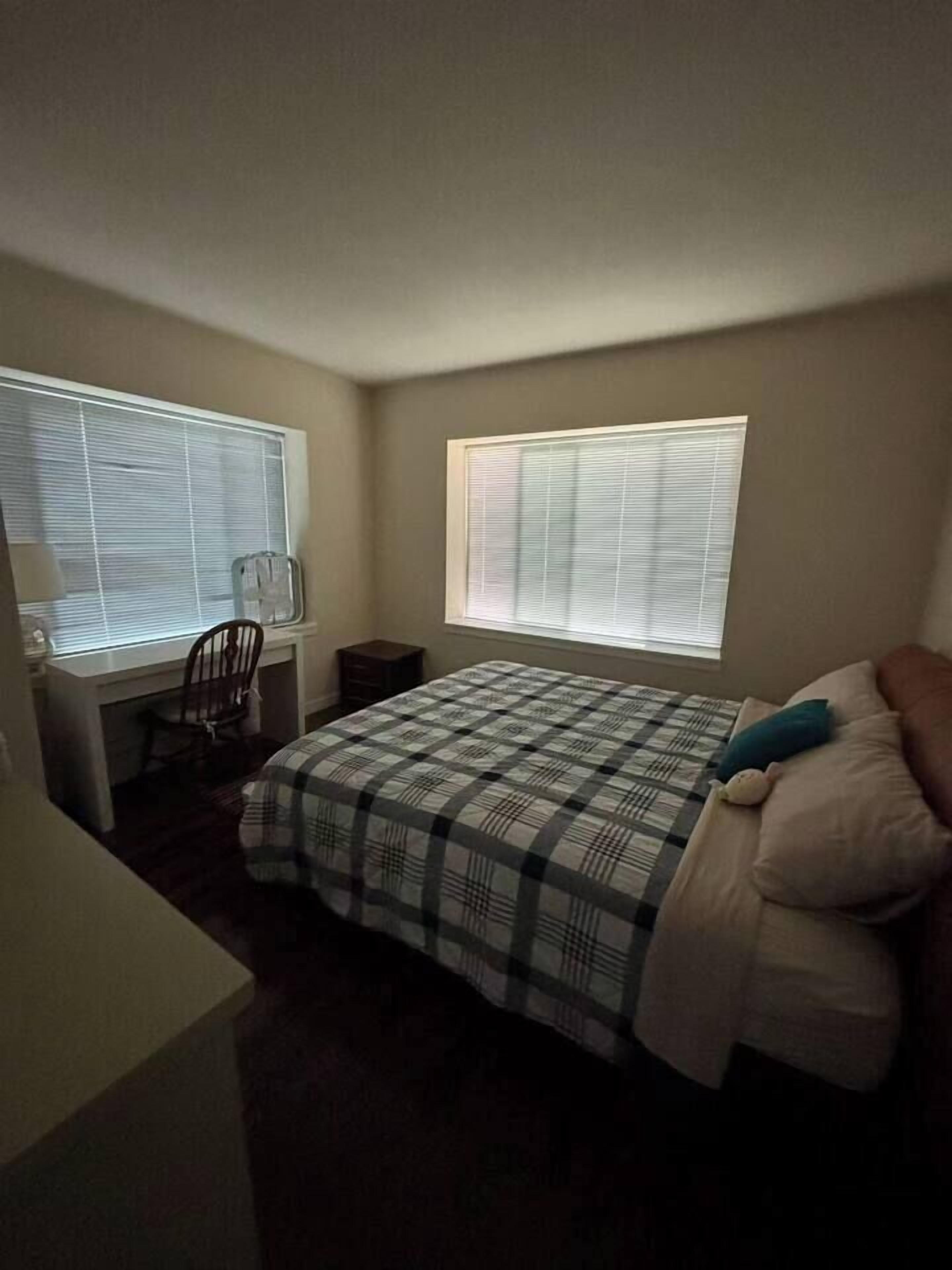 A bedroom with a bed, a desk, and two windows.