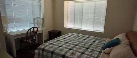 A bedroom with a bed, a desk, and two windows.