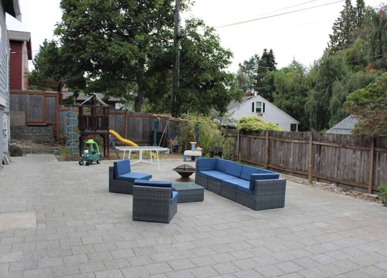 An outdoor patio area with a seating arrangement, a play structure, and a wooden fence.
