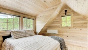 A bedroom with a sloped ceiling, two windows, a bed with a checkered pillow, and an air conditioning unit.