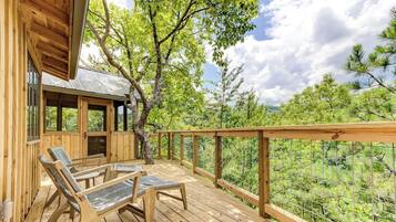 Terraza de madera con dos sillas reclinables y un espacio cubierto con ventanas, con vista a un paisaje boscoso.