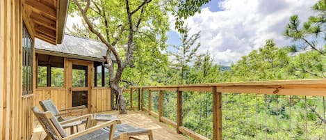 Une terrasse en bois avec deux chaises longues et un espace abrité doté de fenêtres, offrant une vue sur un paysage boisé.