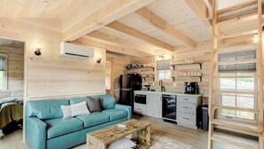 A cozy cabin interior with a sofa, coffee table, kitchen area, and a ladder.