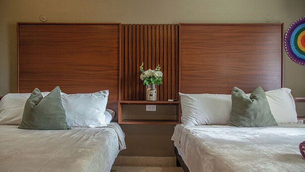 A hotel room with two beds, a wooden headboard, a nightstand with a vase of flowers, and a colorful wall decoration. - Beautiful suite for up to 5 people, with a pool and private parking. (Mérida)